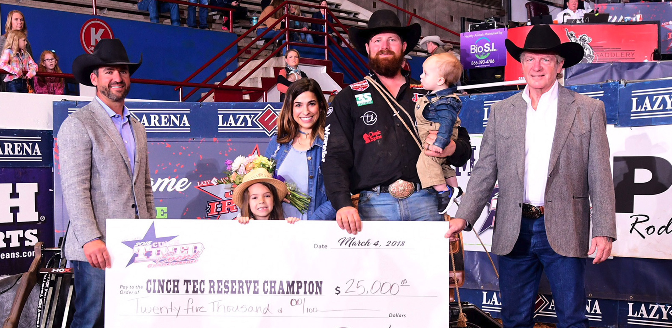 A group of people holding a large white check smiling and posing wearing western attire. 